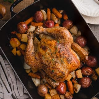 overhead view of a roasted chicken with root vegetables in a cast iron roasting pan