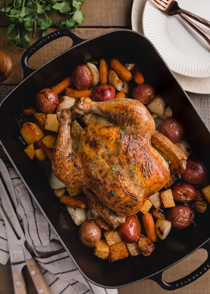 overhead view of a roasted chicken with root vegetables in a cast iron roasting pan