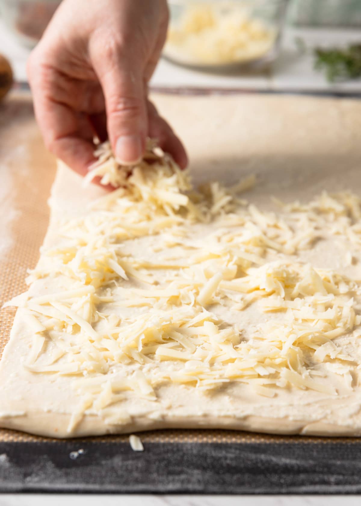 shredded gruyere cheese being sprinkled onto a sheet of puff pastry