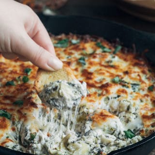 dipping crostini into cheesy warm spinach artichoke dip