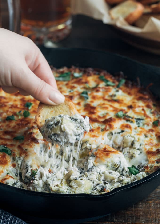 dipping crostini into cheesy warm spinach artichoke dip