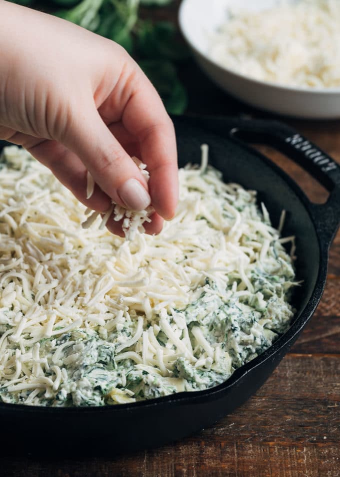 topping unbaked spinach artichoke dip with shredded mozzarella cheese