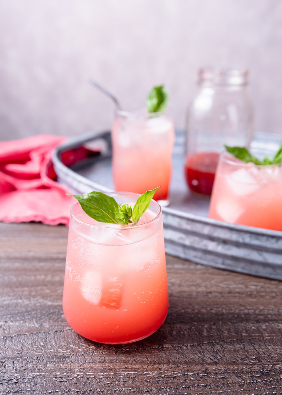 Strawberry Basil Soda served in ice filled glasses on a wood board and metal serving tray