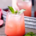 strawberry soda in a glass garnished with basil leaves on a wood board