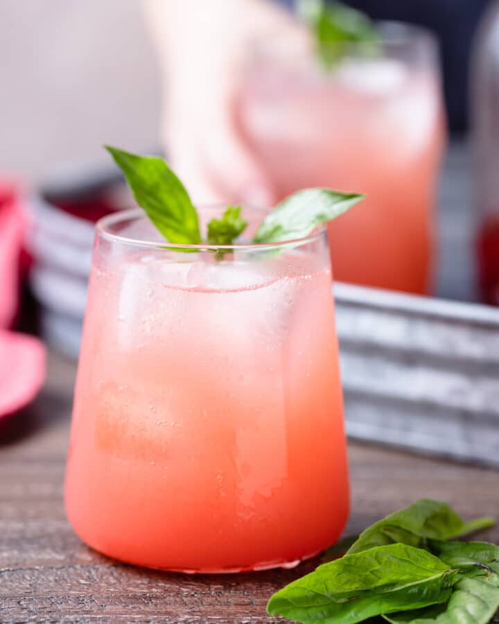 strawberry soda in a glass garnished with basil leaves on a wood board