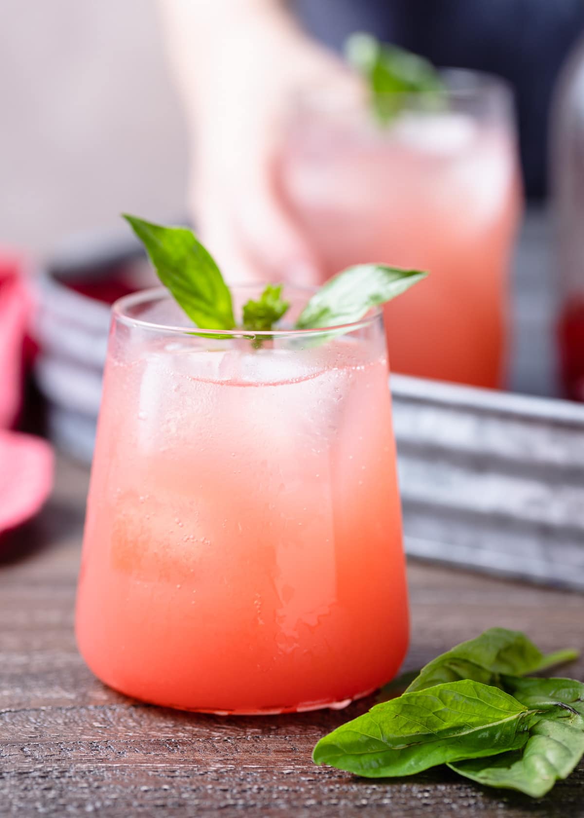 strawberry soda in a glass garnished with basil leaves on a wood board