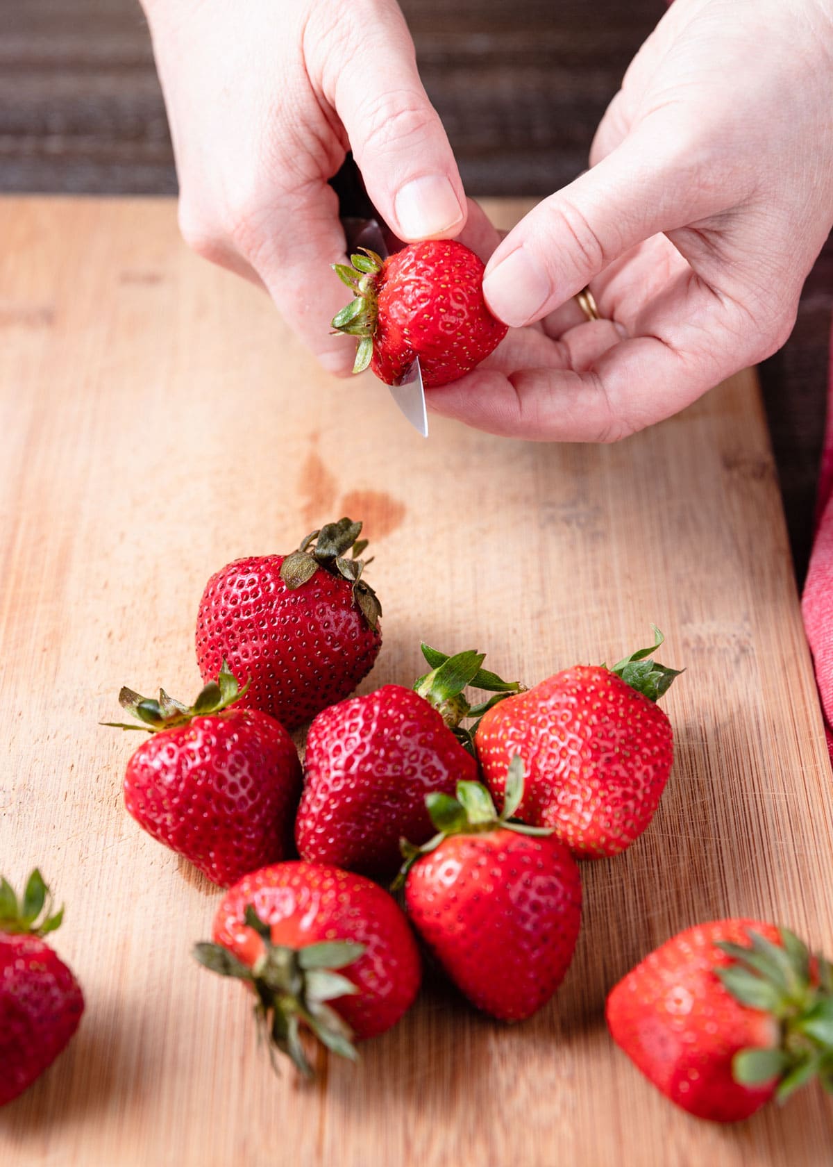 slicing strawberries with a paring knife over a wood cutting board