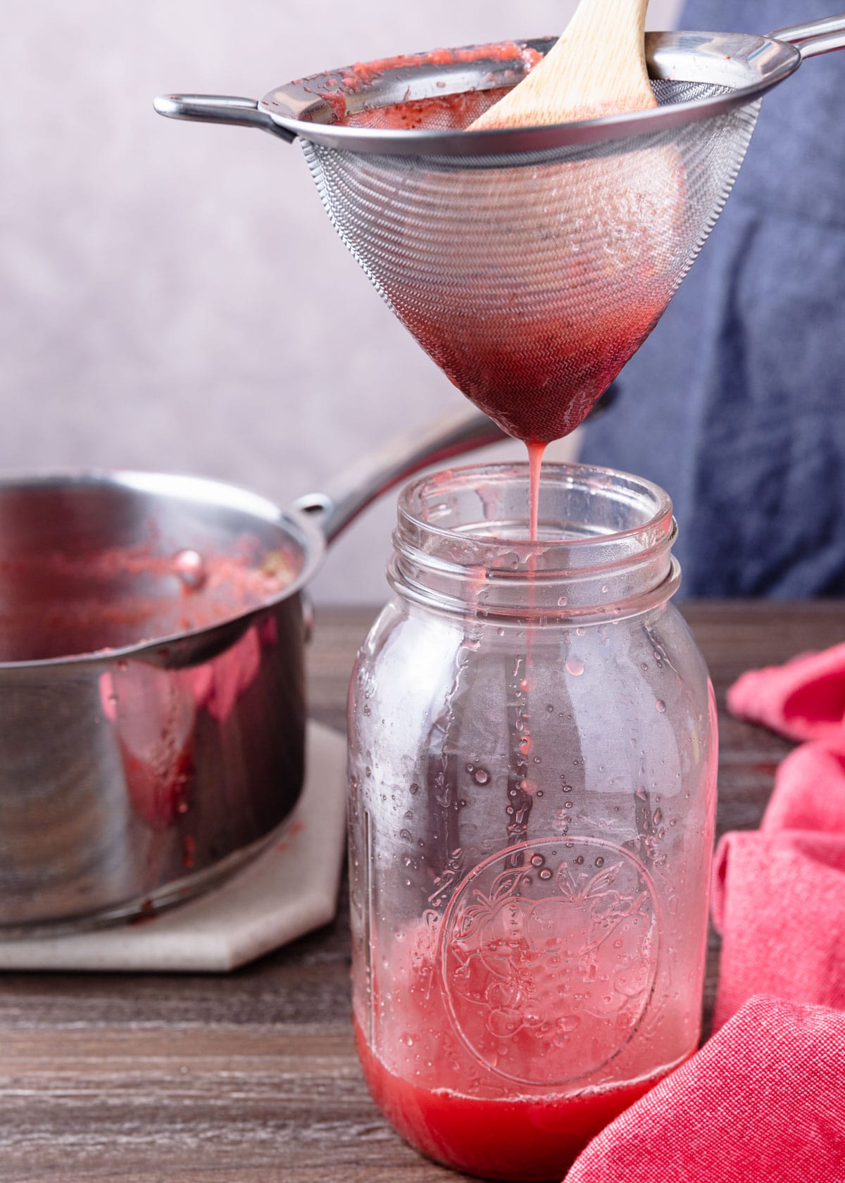 straining strawberry syrup in a conical mesh sieve into a glass jar