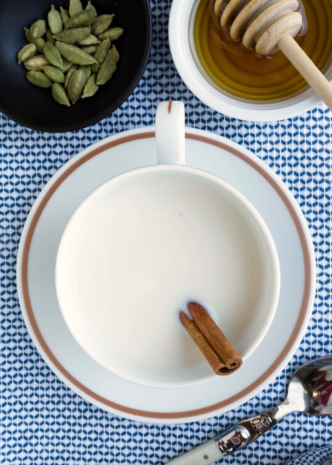 overhead photo of cardamom-spiced milk in a teacup on a blue and white napkin