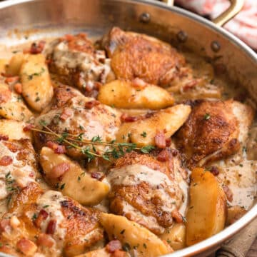 side view of hard cider chicken with bacon and apples in a copper frying pan