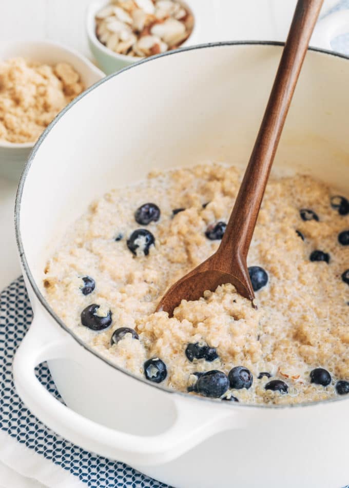 cooked breakfast quinoa with blueberries in a white pot with a wooden spoon