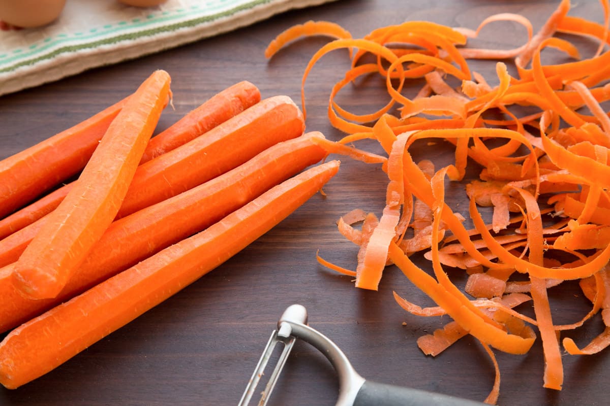 whole carrots and peels on a dark wood cutting board
