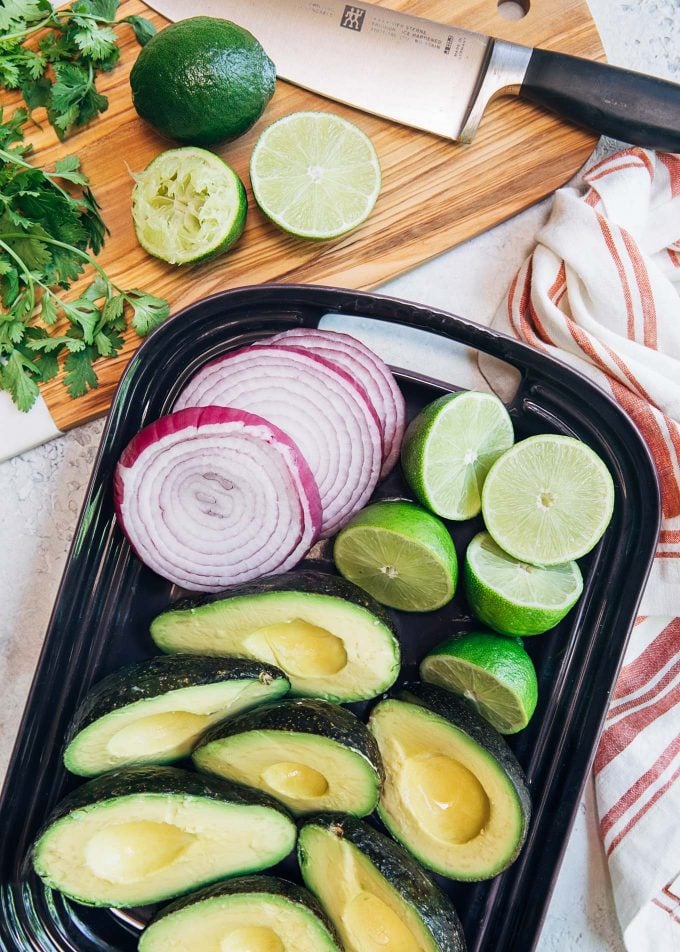 avocados, onions, and limes on a platter for grilled guacamole