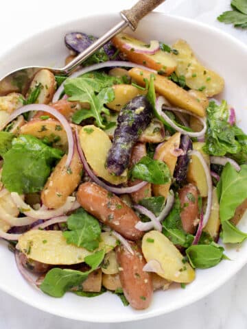 fingerling potato salad in a white bowl with a serving spoon