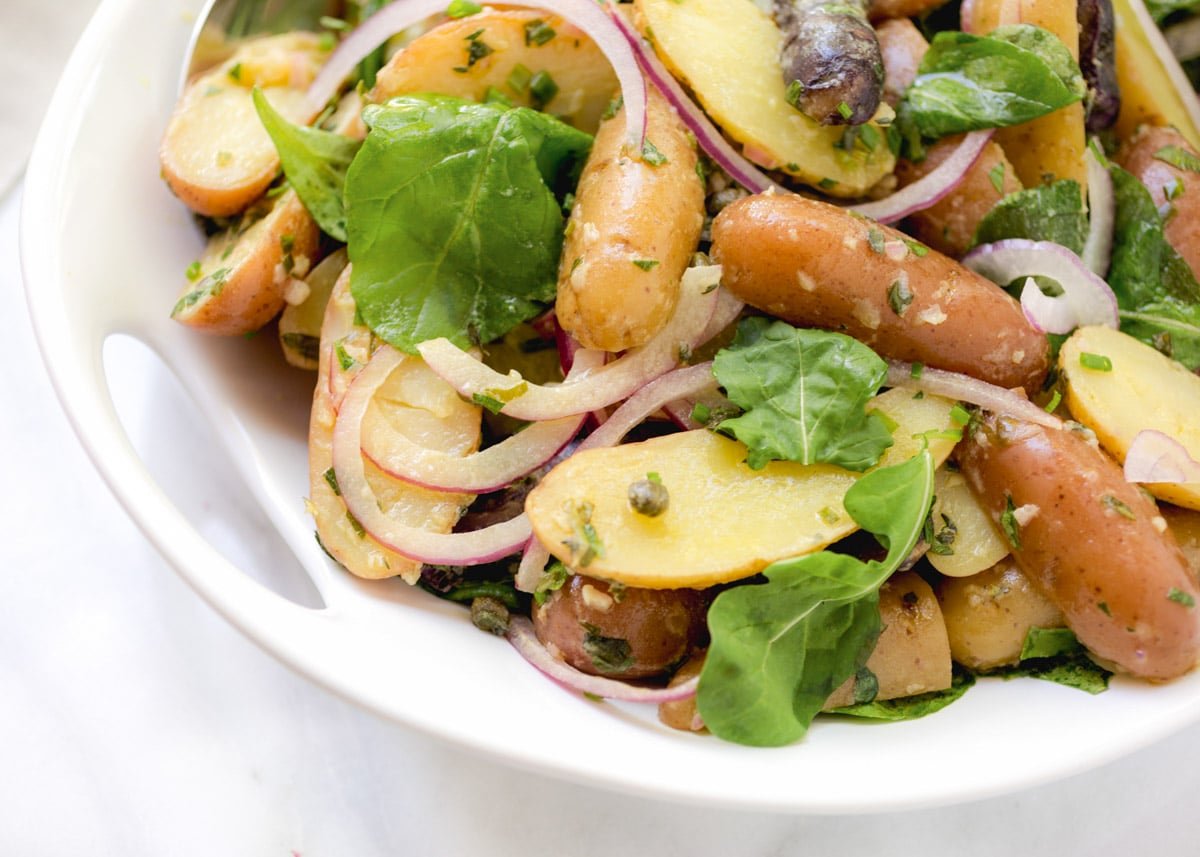 closeup of fingerling potato salad with red onions and baby arugula in a white serving bowl
