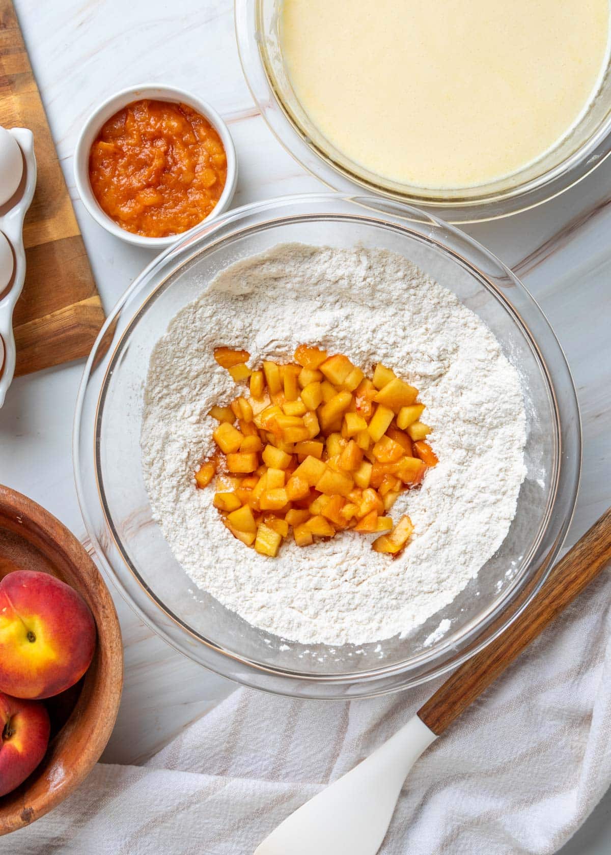 Diced fresh peaches tossed with the flour mixture in a large glass bowl before being combined with the prepared wet ingredients for peach muffins.