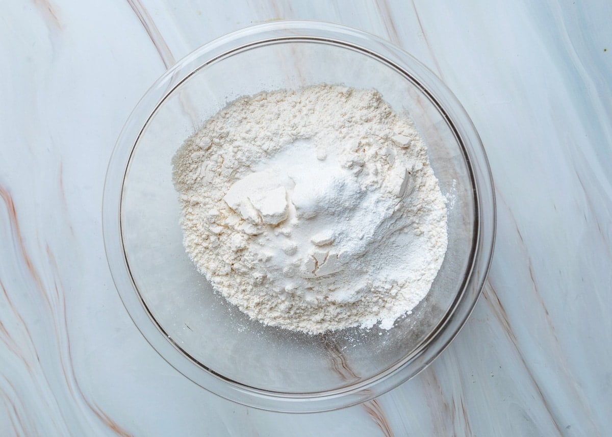 Overhead view of flour, baking powder, and salt combined in a glass mixing bowl, ready to be whisked together for the muffin batter.