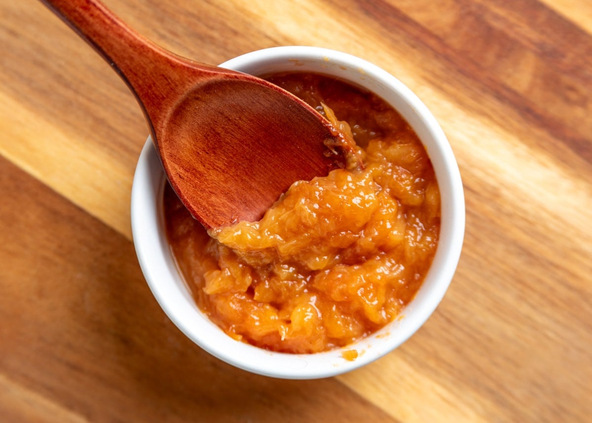 Close-up of cooked peach filling in a white ramekin with a wooden spoon scooping up the thick, glossy mixture, showing its soft, jam-like texture.