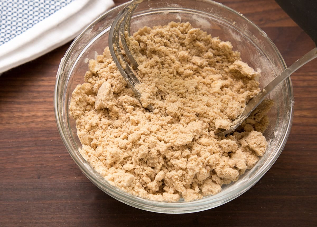Overhead view of cinnamon streusel topping after mixing, showing a crumbly texture with small and medium-sized butter crumbs in a glass bowl.