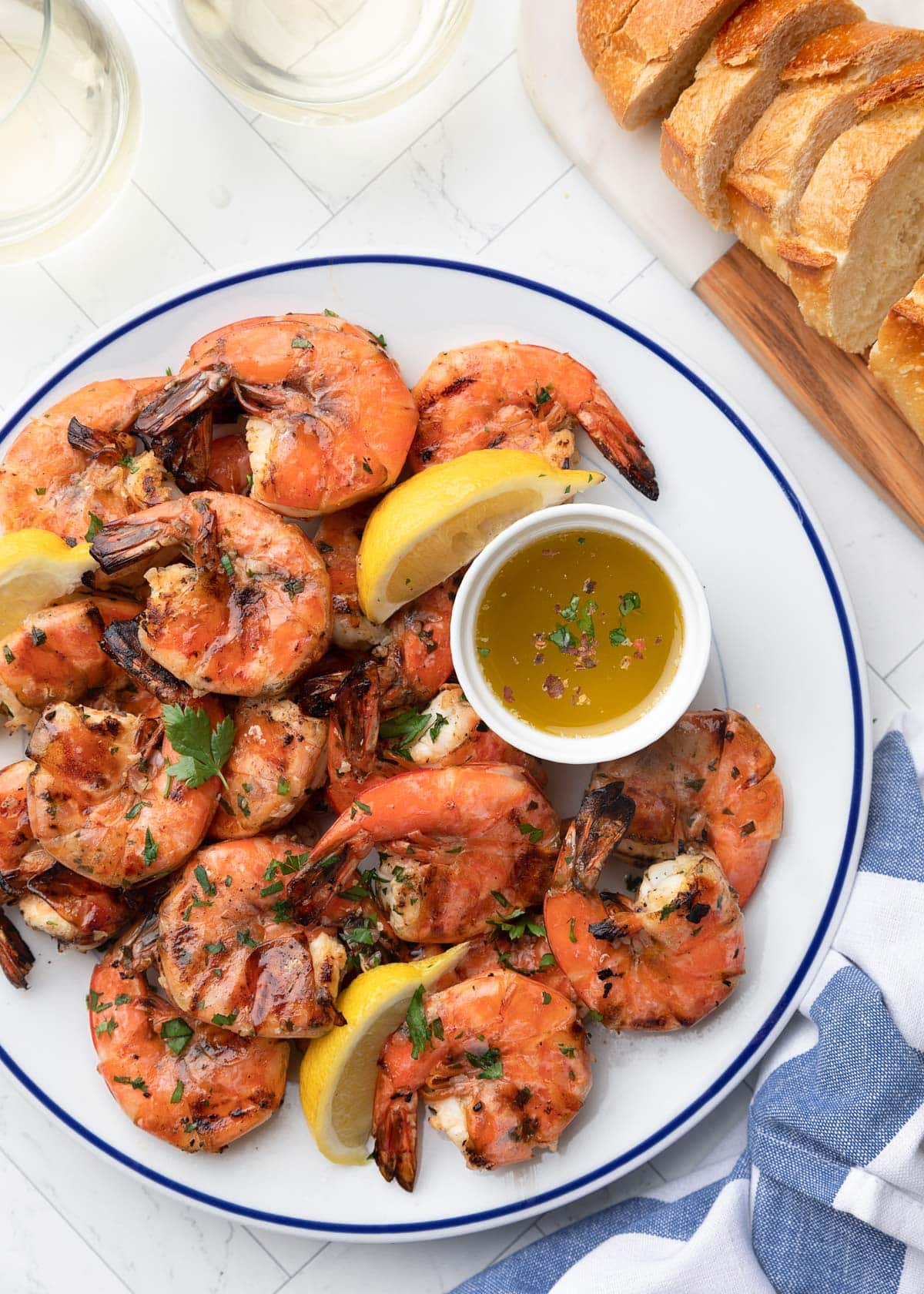 grilled lemon garlic shrimp on a blue rimmed white plate with lemon wedges and a bowl of dipping butter