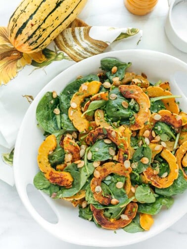 delicata squash salad with baby spinach and brown butter vinaigrette in a white serving bowl