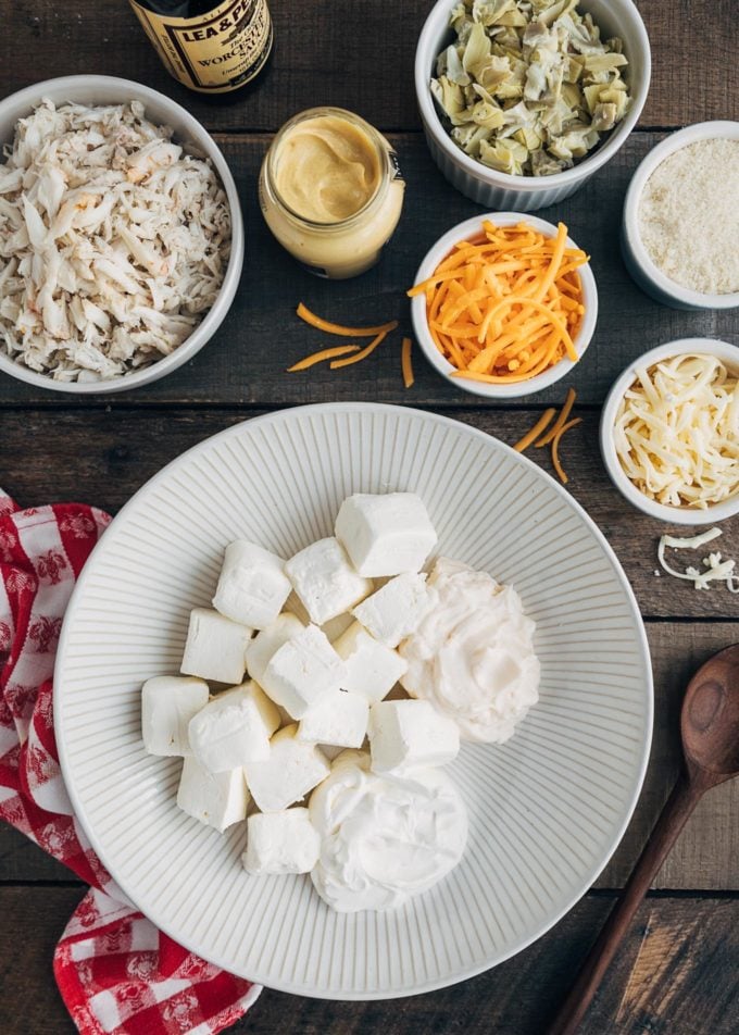 ingredients for crab and artichoke dip in bowls on a wood board