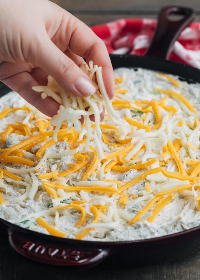 sprinkling cheese onto crab and artichoke dip in a cast iron skillet