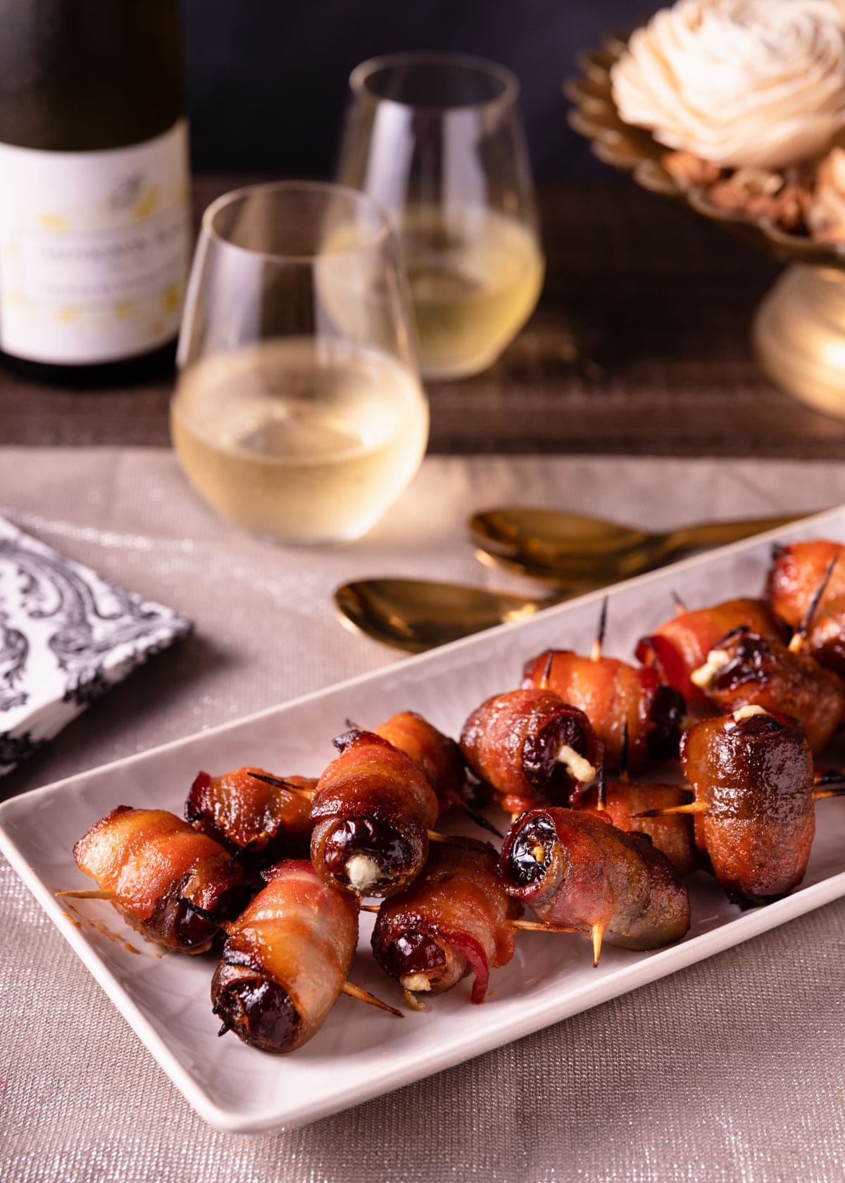 maple sriracha devils on horseback on a white serving platter surrounded by napkins and glasses of wine