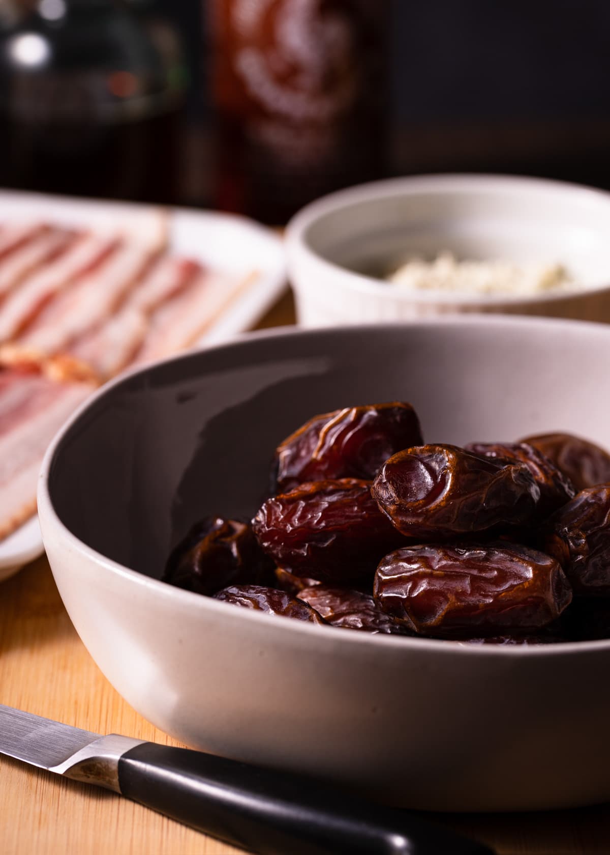 a bowl of medjool dates with a bowl of crumbled blue cheese and a platter of raw bacon in the background