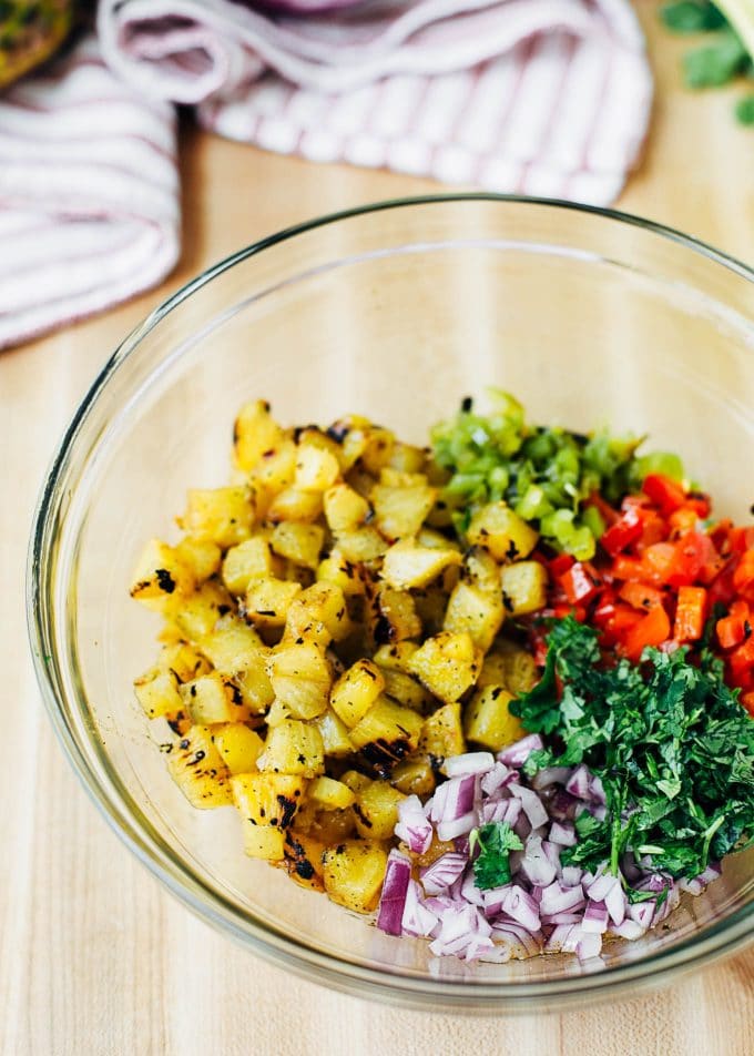 mixing grilled pineapple with peppers, onions, and cilantro in a bowl