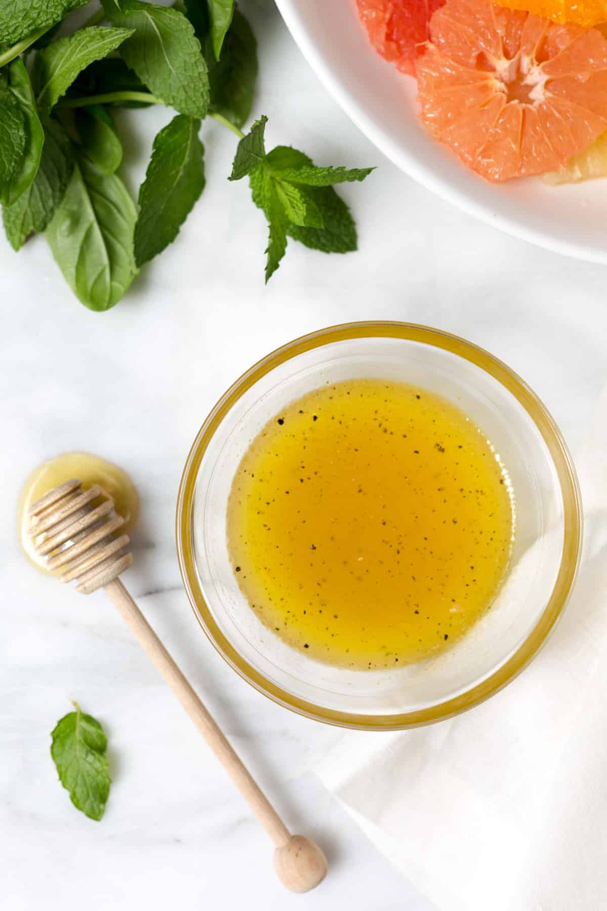 overhead photo of honey balsamic vinaigrette in a glass bowl next to a honey dipper on a white marble board