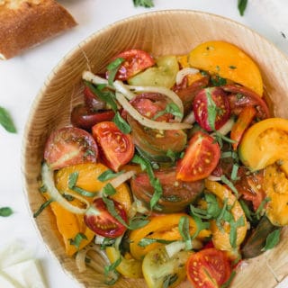 heirloom tomato salad with onions and basil in a wooden bowl