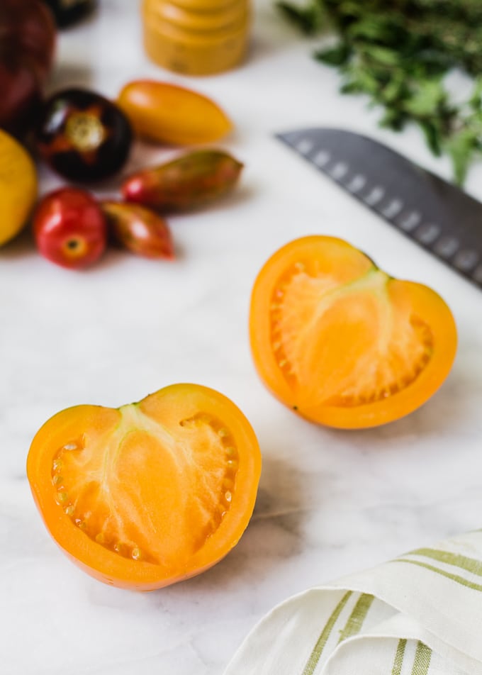 halved orange tomato on a marble board with a santoku knife