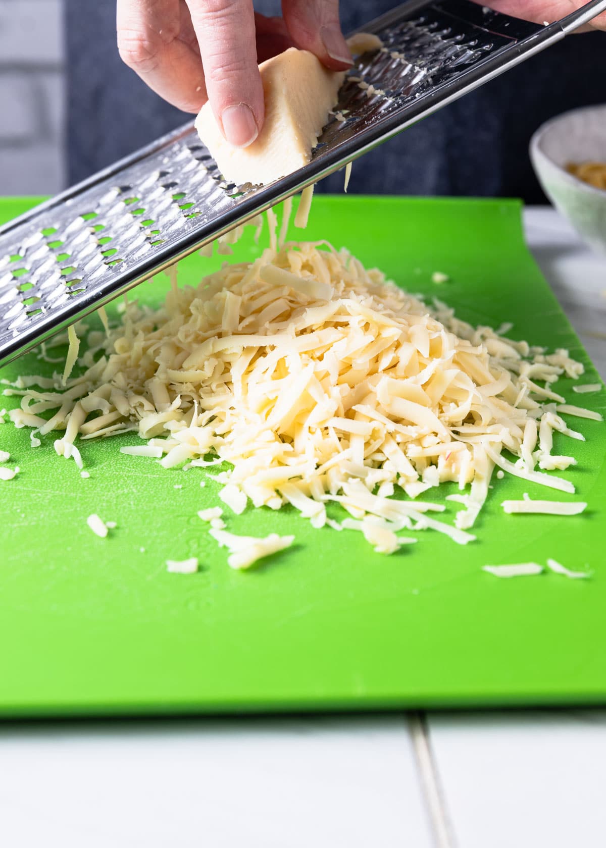 grating fontina cheese on a green cutting board