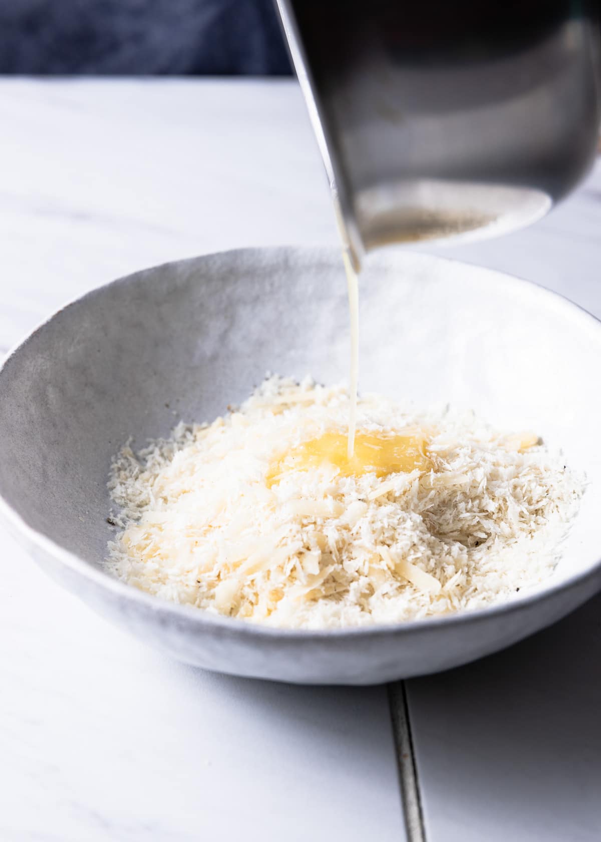 drizzlilng melted butter into a white bowl filled with panko breadcrumbs and parmesan cheese
