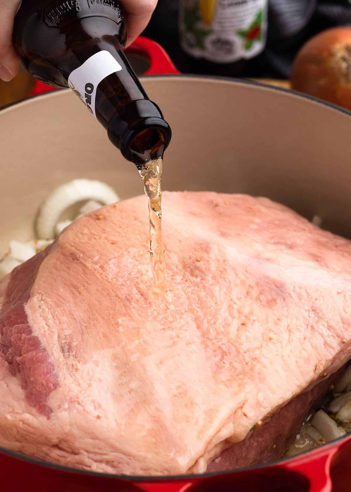 pouring beer over a corned beef brisket in an enameled cast iron Dutch oven