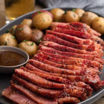 sliced beer braised corned beef with whiskey mustard glaze on a gray ceramic platter with baby potatoes