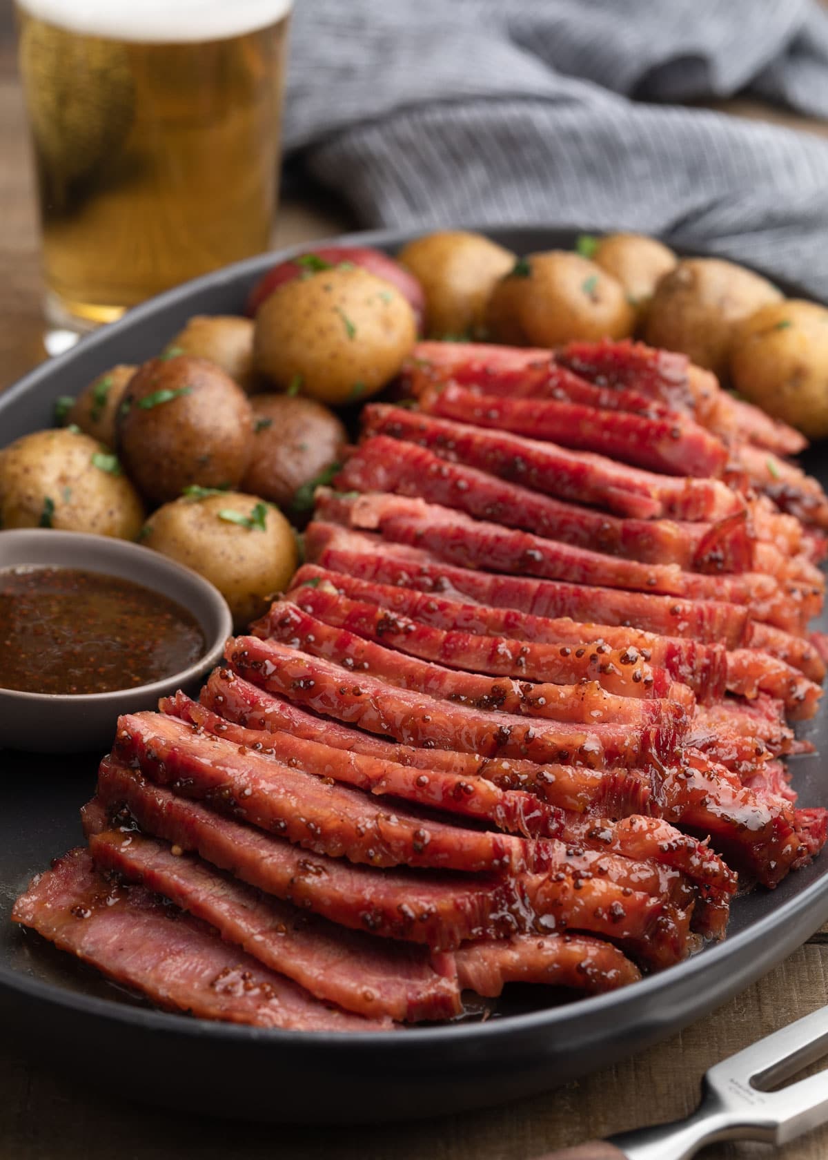 sliced beer braised corned beef with whiskey mustard glaze on a gray ceramic platter with baby potatoes
