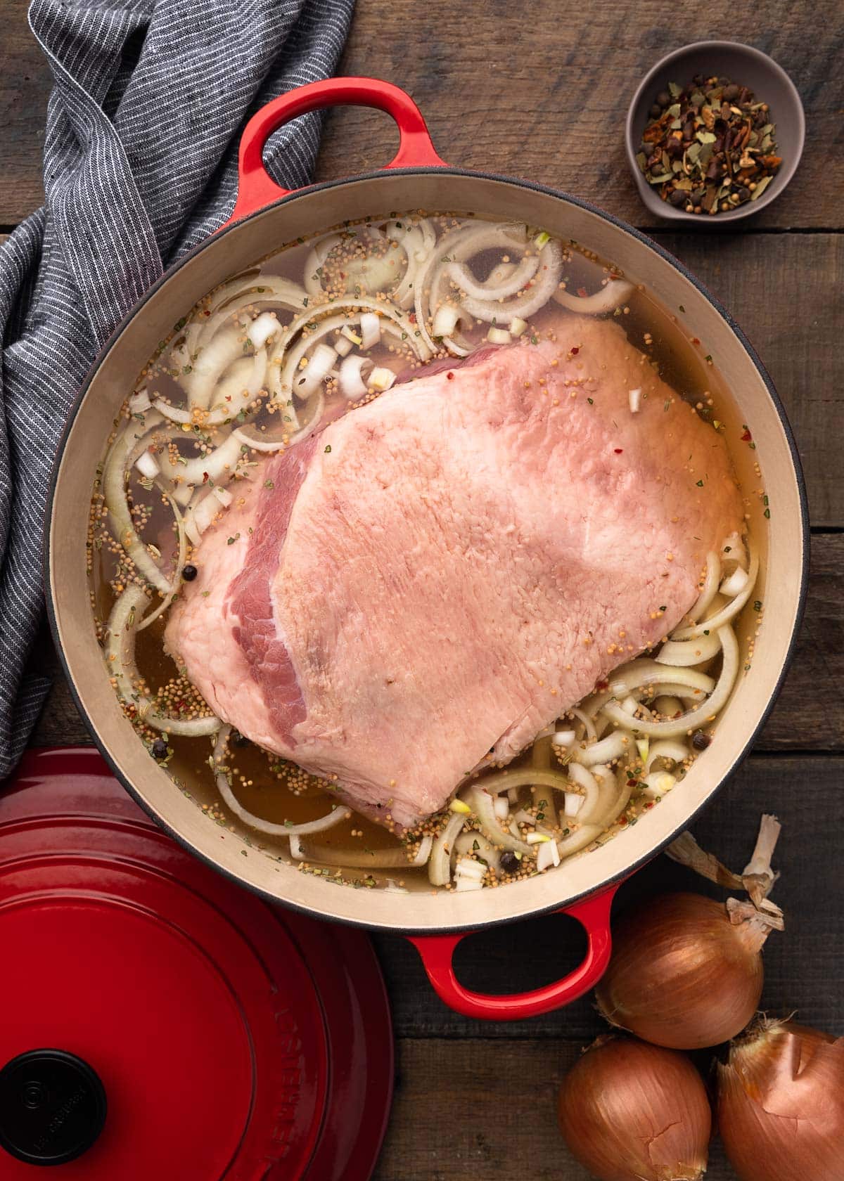 overhead of a corned beef brisket in an enameled cast iron pot, with onions, garlic, and beer