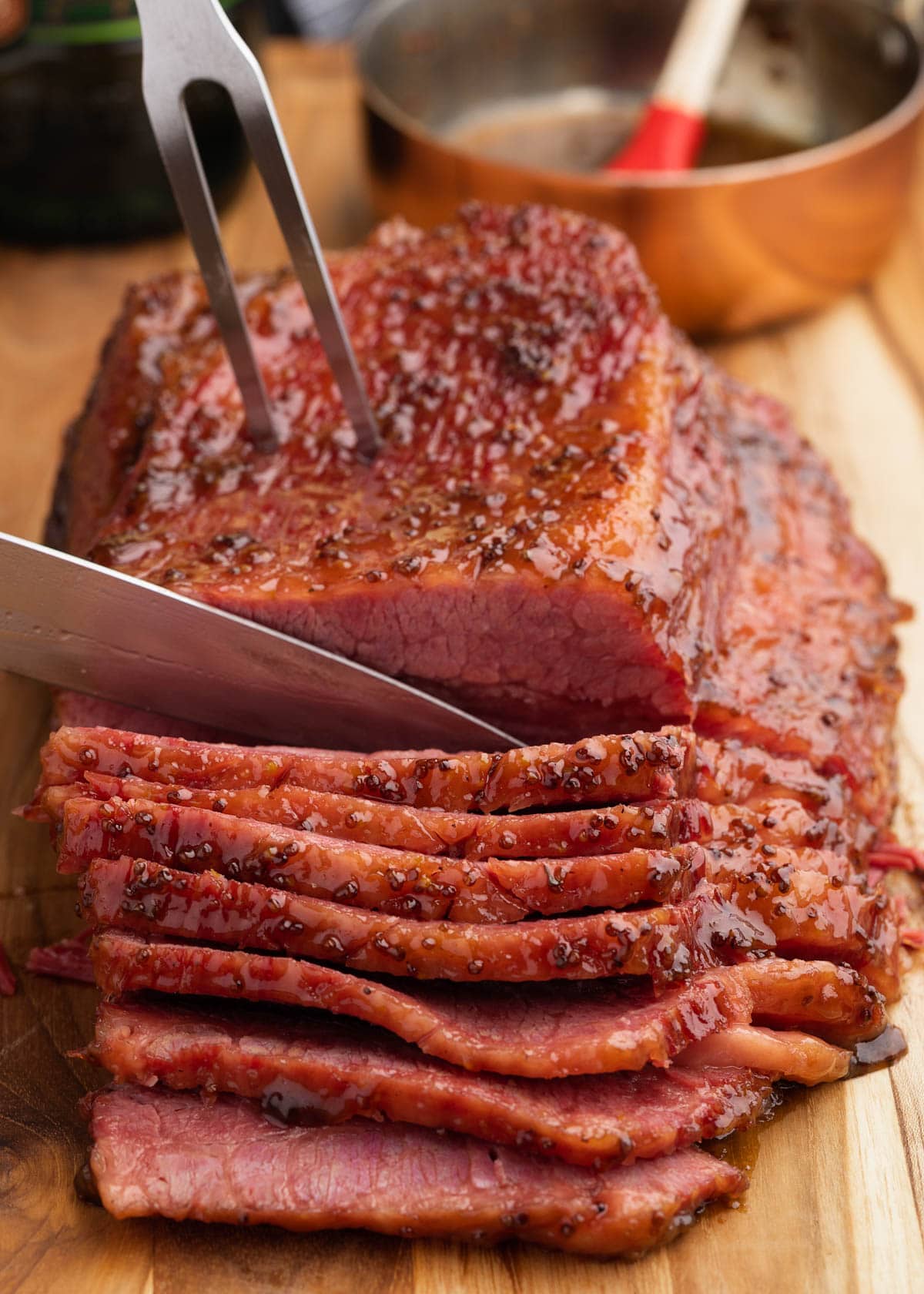 glazed corned beef on a wood cutting board being sliced with a knife and meat fork