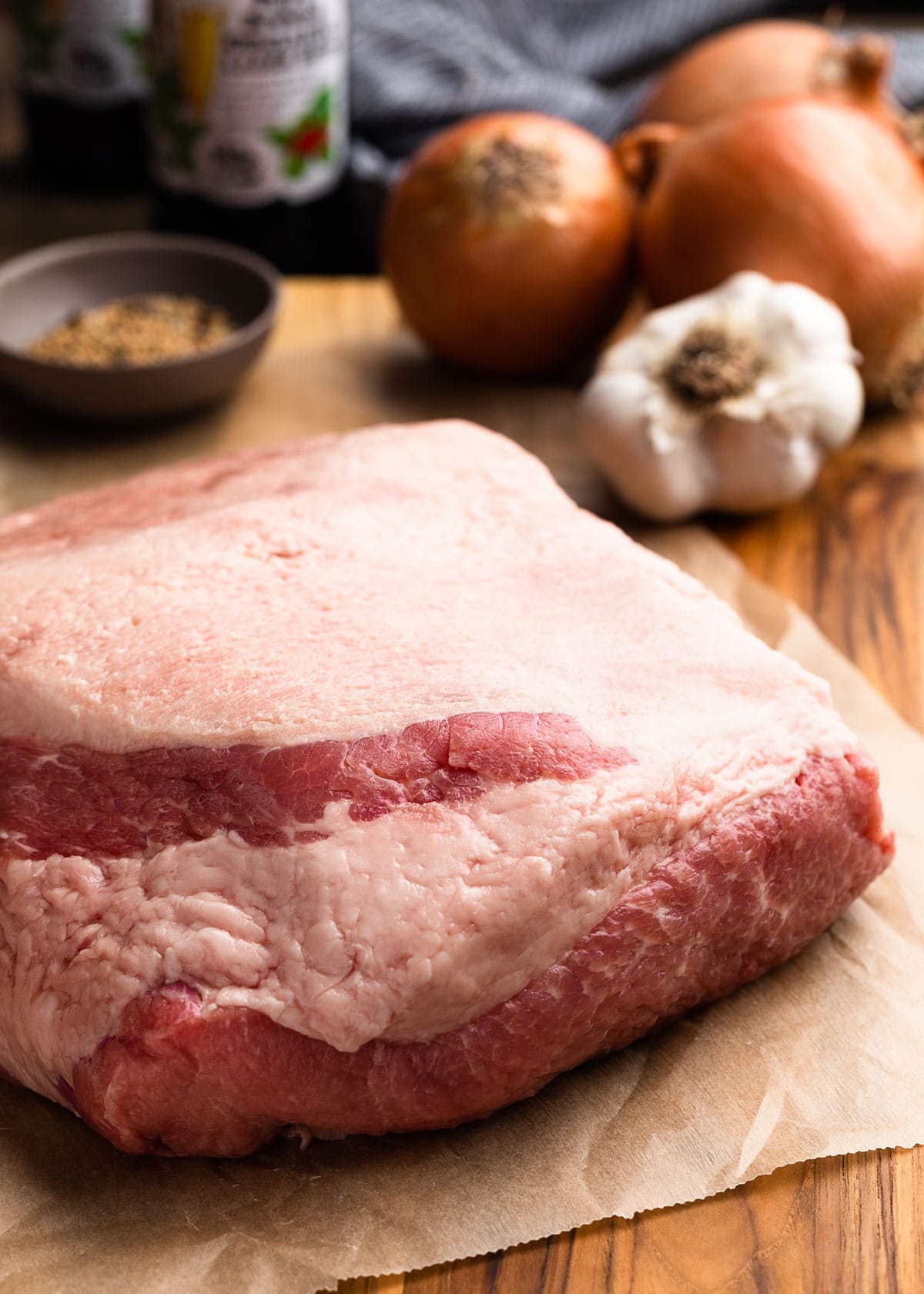 uncooked corned beef brisket on a parchment lined wood cutting board with onions and garlic