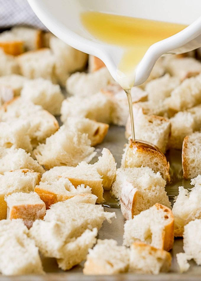 pouring garlic butter onto French bread cubes for croutons