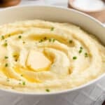 cream cheese mashed potatoes in a white serving bowl with pats of butter and snipped chives