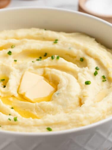 cream cheese mashed potatoes in a white serving bowl with pats of butter and snipped chives