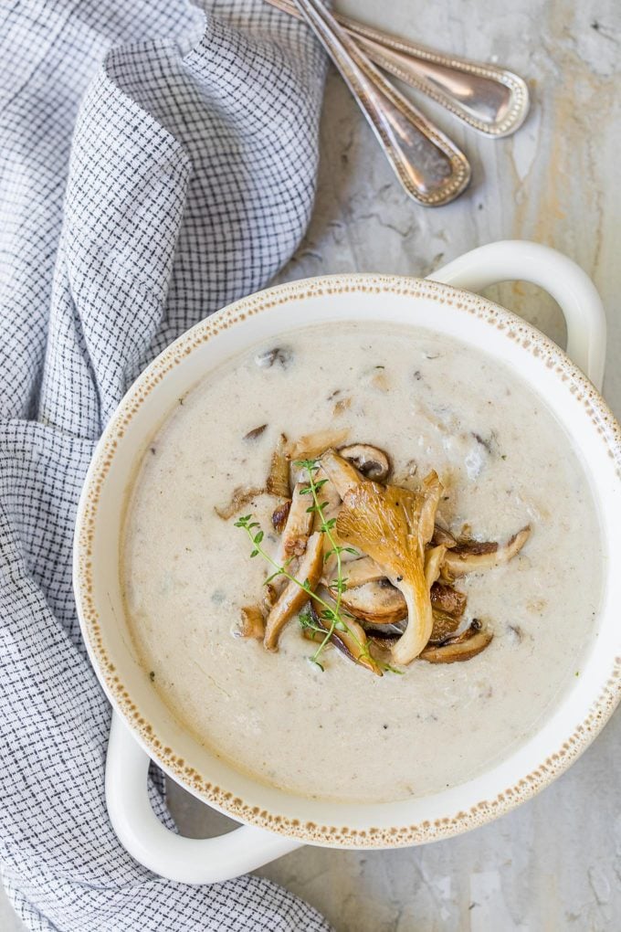 overhead photo of homemade cream of mushroom soup in a white bowl with a blue checked napkin