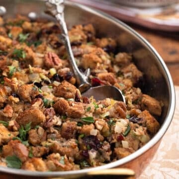 side view of baked cranberry pecan stuffing in a gratin dish with a silver serving spoon