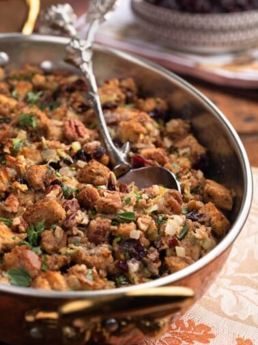 side view of baked cranberry pecan stuffing in a gratin dish with a silver serving spoon