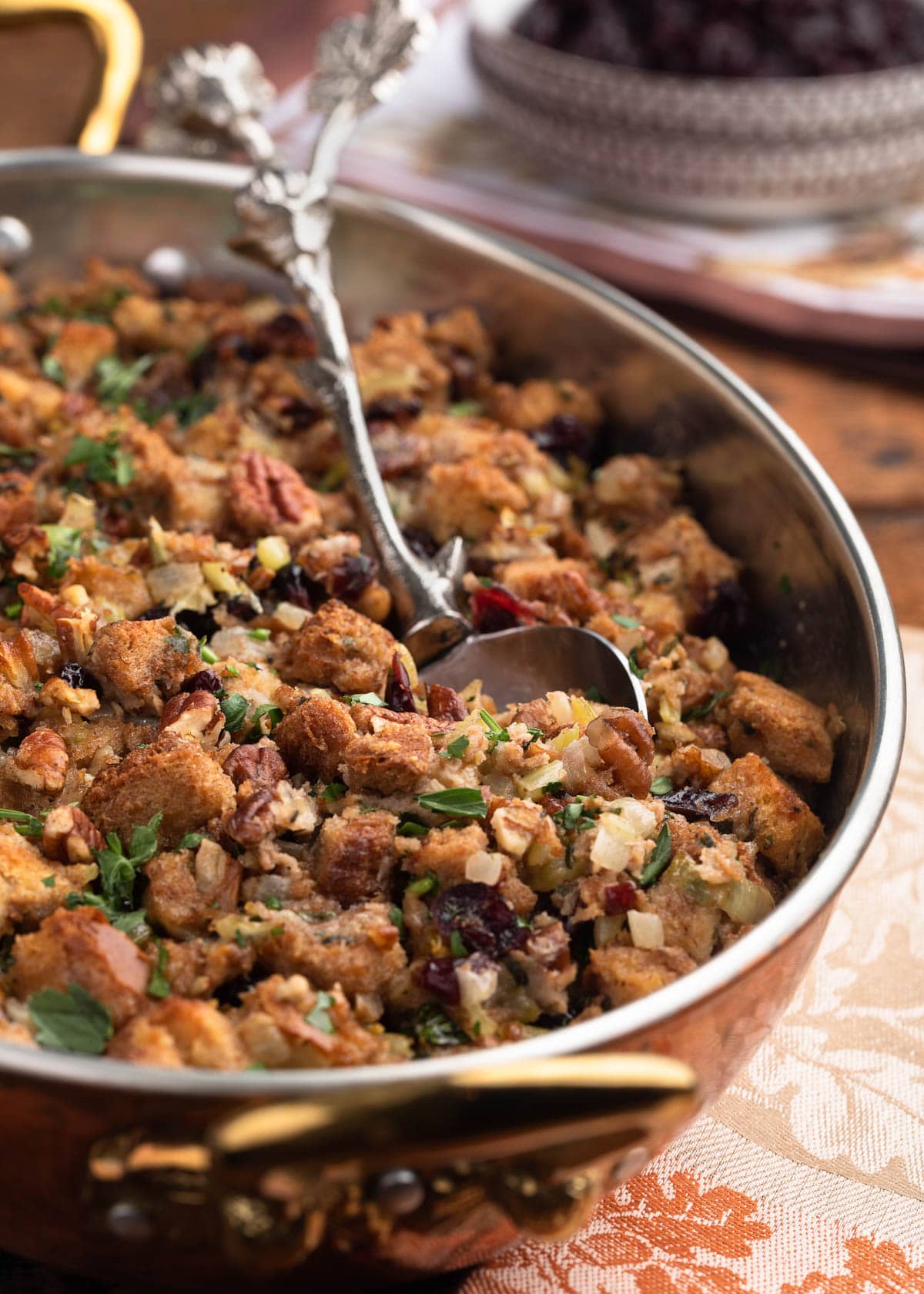 side view of baked cranberry pecan stuffing in a gratin dish with a silver serving spoon