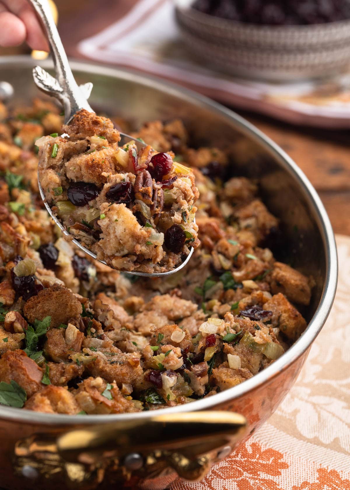 silver serving spoon holding a scoop of cranberry pecan stuffing over the baking dish