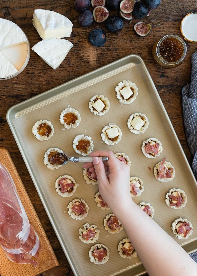 spooning fig jam into miniature phyllo shells on a baking sheet